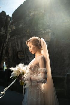 A bride in a white dress with a bouquet of flowers on the background of mountains and gorges in the Swiss Saxony, Germany, Bastei.