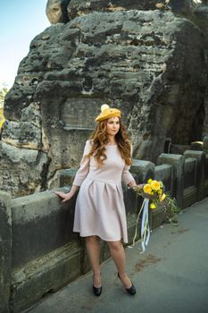 a girl in a pink dress and a hat with a bouquet of flowers on the background of mountains and gorges in Swiss Saxony, Germany, Bastei.