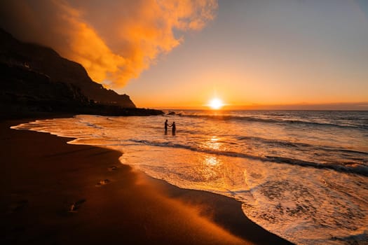 A couple in love stands in the ocean in the evening looking at the beautiful sunset on the island of Tenerife.Spain.