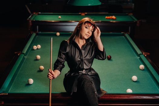 A girl with glasses sits on a pool table in a club.Russian billiards.