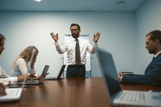 Chief holds business meeting in modern office. Employees sit at table using laptops. Toned image. Close up shot. High quality photo.