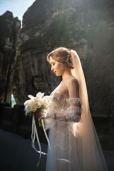 A bride in a white dress with a bouquet of flowers on the background of mountains and gorges in the Swiss Saxony, Germany, Bastei.