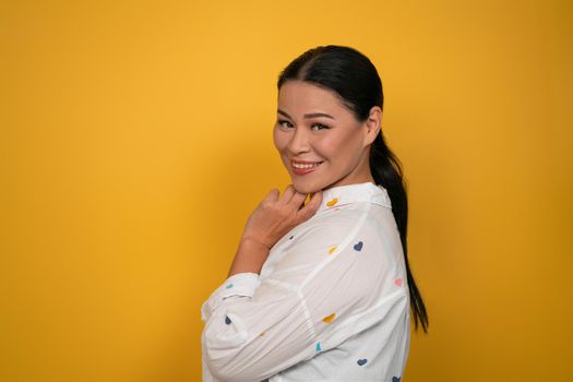 Charming Asian woman smiling at camera. Cute middle aged female model cutout on yellow background. Copy space.