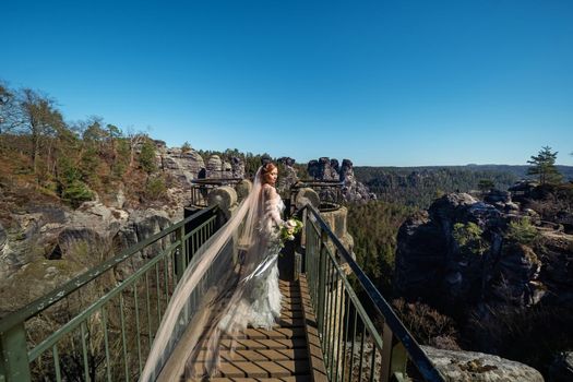 A bride in a white dress with a bouquet of flowers on the background of mountains and gorges in the Swiss Saxony, Germany, Bastei.