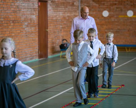 First graders in their first physical education class at the gym. The teacher assigns a task to the students. Moscow, Russia, September 2, 2019