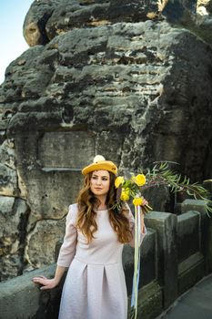 a girl in a pink dress and a hat with a bouquet of flowers on the background of mountains and gorges in Swiss Saxony, Germany, Bastei.