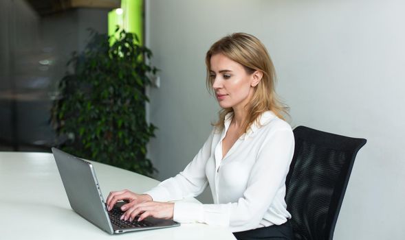 Pretty businesswoman working with computer in office. Young Caucasian lady typing at laptop.