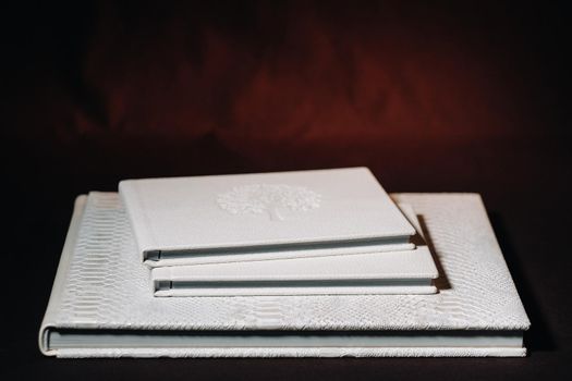 Composition of photo books in natural white leather of different sizes. The white paper on a dark background