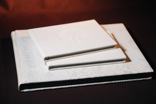 Composition of photo books in natural white leather of different sizes. The white paper on a dark background