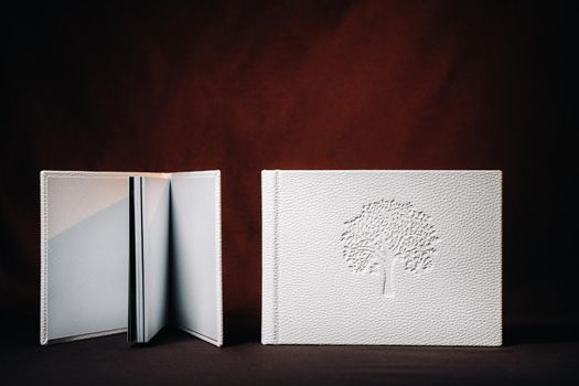 Composition of photo books in natural white leather of different sizes. The white paper on a dark background