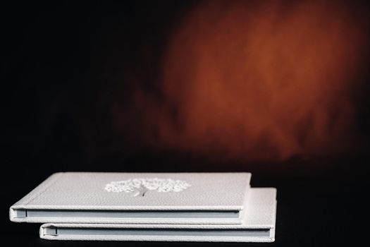 Composition of photo books in natural white leather of different sizes. The white paper on a dark background