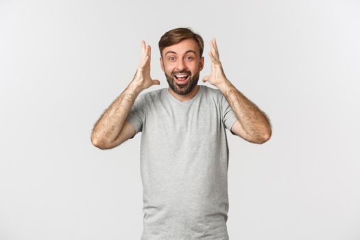 Image of excited happy guy hearing amazing news, standing over white background and smiling.