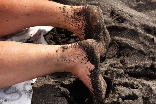 Close-up of a woman's legs and feet in the sand, lying on the volcanic black sand on the beach.Tenerife.