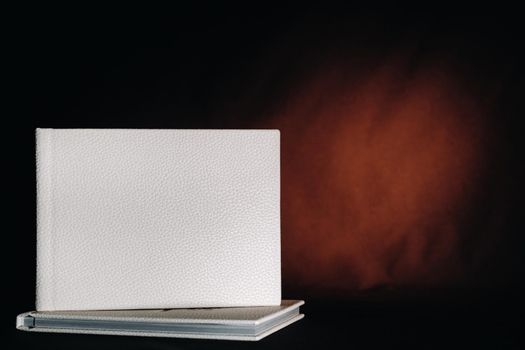 Composition of photo books in natural white leather of different sizes. The white paper on a dark background