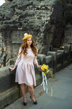 a girl in a pink dress and a hat with a bouquet of flowers on the background of mountains and gorges in Swiss Saxony, Germany, Bastei.