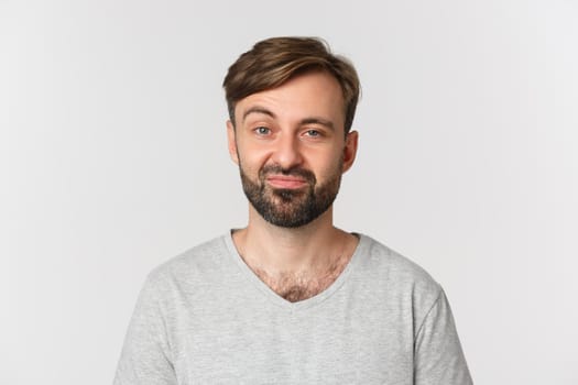 Close-up of skeptical and unamused bearded man, wearing gray t-shirt, standing over white background.