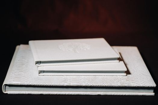 Composition of photo books in natural white leather of different sizes. The white paper on a dark background