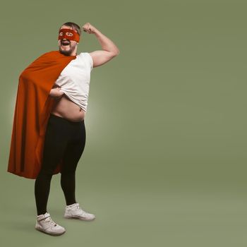 Body positive Super hero man shows his muscles and tummy. Super power and overweight concept. Isolated on green background with text space at right side. Template for social networks.