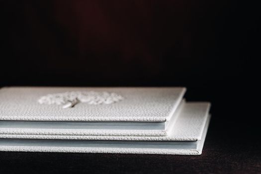Composition of photo books in natural white leather of different sizes. The white paper on a dark background