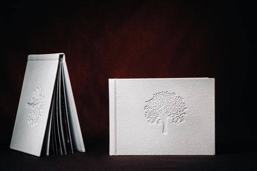 Composition of photo books in natural white leather of different sizes. The white paper on a dark background