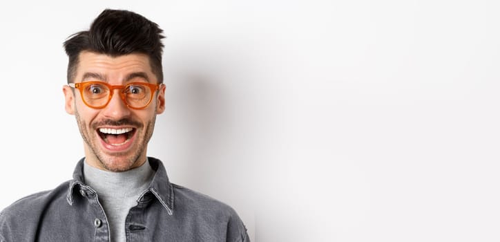 Excited handsome man in trendy eyewear checking out awesome promo, smiling amused, standing happy on white background.