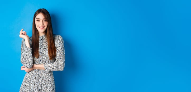 Beautiful caucasian woman 25s wearing dress, standing against blue background and smiling confident.