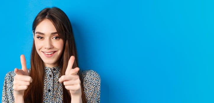 Excited and confident beauty woman, pointing fingers at camera and smiling, invite and beckon you, join us gesture, praising good choice, standing on blue background.