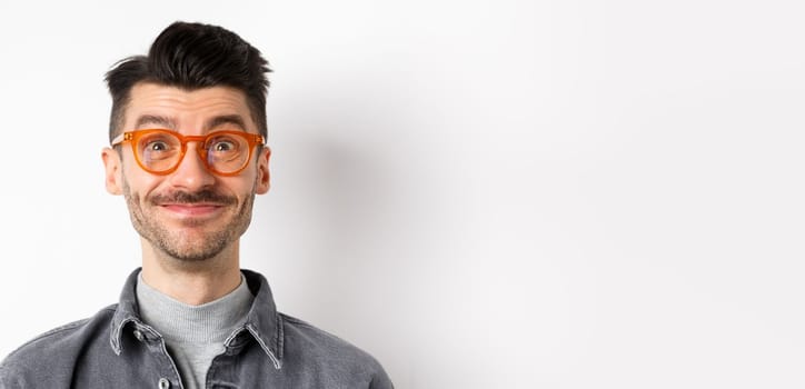 Close-up of happy man with moustache and glasses looking at camera, smiling pleased, standing against white background.