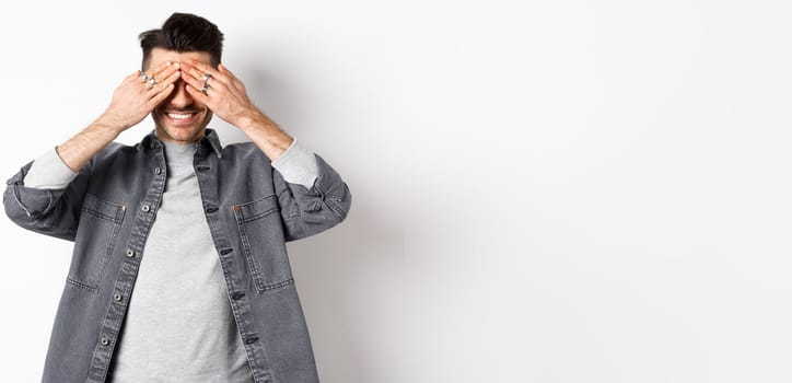 Happy smiling guy waiting with closed eyes for surprise, standing excited on white background.