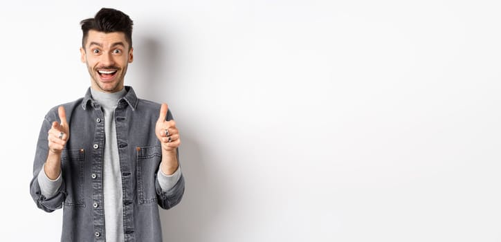 Excited young man showing thumbs-up and smiling happy, praise good thing, motivating you, recommending cool product, standing on white background.