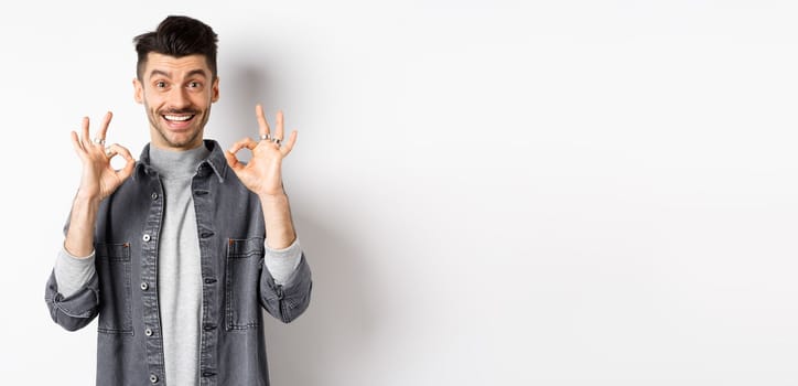 Happy guy say yes, smiling and showing okay signs, like good product, nod in approval and make satisfied face, praise excellent work, standing on white background.