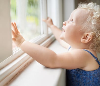 Discovering the world. A cute baby girl peering out of the window