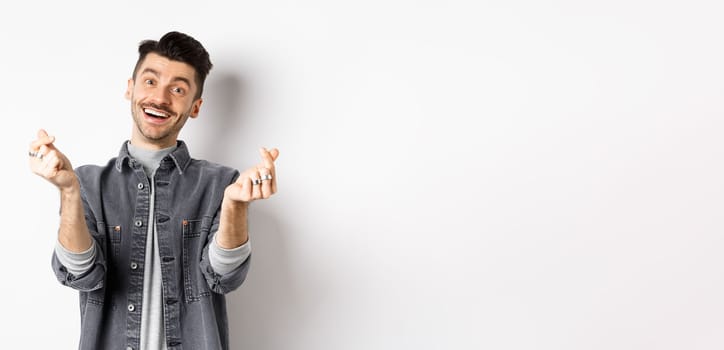 Handsome smiling man showing hand hearts and looking with love at camera, standing on white background.