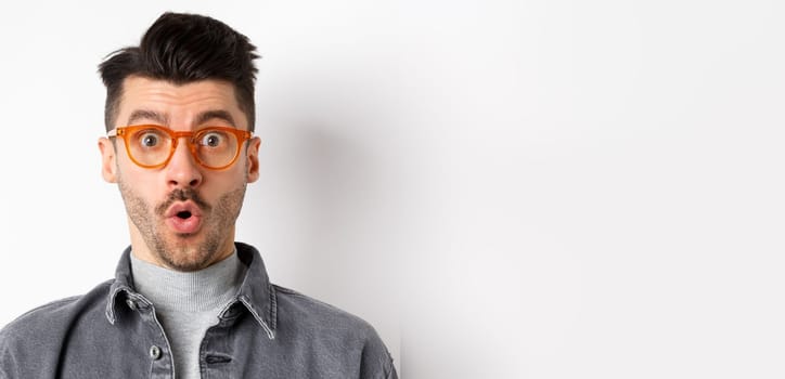 Wow look there. Excited handsome man in stylish glasses stare impressed at camera, checking out eyewear store offer, standing on white background.