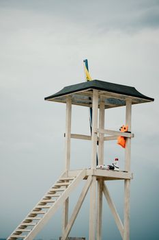 Empty white lifeguard tower with a yellow flag on the beach in windy weather. Beach lifeguard tower with yellow flag indicator. Nobody. Holiday recreation concept