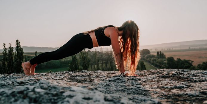 Well looking middle aged woman with long hair, fitness instructor in leggings and tops doing stretching and pilates on the rock near forest. Female fitness yoga routine concept. Healthy lifestyle.