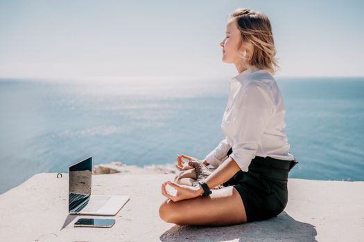 Happy girl doing yoga with laptop working at the beach. beautiful and calm business woman sitting with a laptop in a summer cafe in the lotus position meditating and relaxing. freelance girl remote work beach paradise