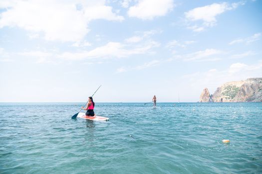 Woman sup yoga. Happy young sporty woman practising yoga pilates on paddle sup surfboard. Female stretching doing workout on sea water. Modern individual female outdoor summer sport activity