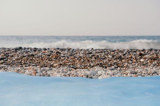 Blue yoga mat is on a sandy beach by the sea