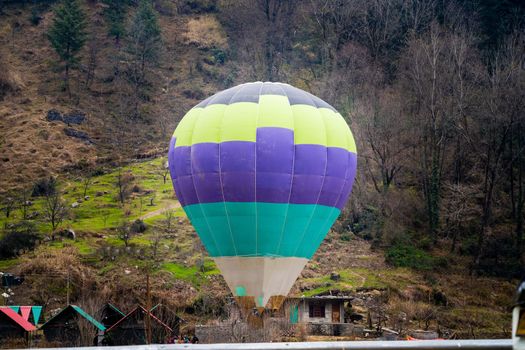 Hot air balloon with fire heating air in wicker basket with himalaya mountains in background showing this adventure in kullu manali valley India