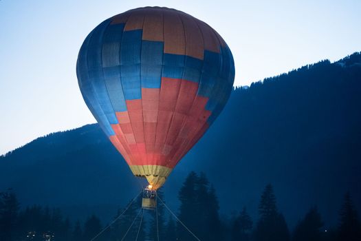 Hot air balloon with fire heating air in wicker basket with himalaya mountains in background showing this adventure in kullu manali valley India