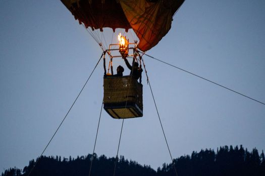 Close up shot of basket of Hot air balloon with fire heating air in wicker basket with himalaya mountains in background showing this adventure in kullu manali valley