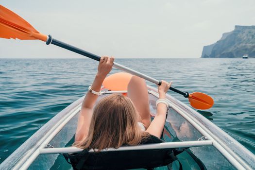 Woman in kayak back view. Happy young woman with long hair floating in transparent kayak on the crystal clear sea. Summer holiday vacation and cheerful female people having fun on the boat.