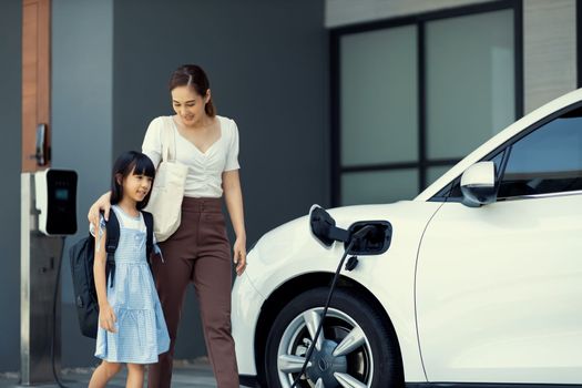 Progressive lifestyle of mother and daughter who have just returned from school in an electric vehicle that is being charged at home. Electric vehicle powered by sustainable clean energy.