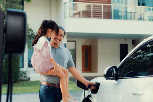 Progressive father and daughter returned from school in electric vehicle that is being charged at home. Electric vehicle driven by renewable clean energy. Home charging station concept for environment