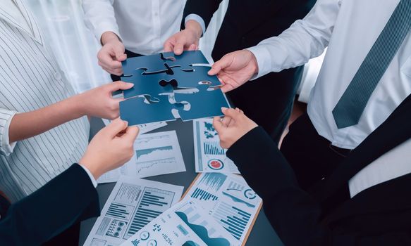 Closeup top view business team of office worker putting jigsaw puzzle together over table filled with financial report paper in workplace with manager to promote harmony concept in meeting room.