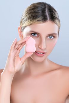 Alluring beautiful female model applying powder puff for facial makeup concept. Portrait of flawless perfect cosmetic skin woman put powder foundation on her face in isolated background.