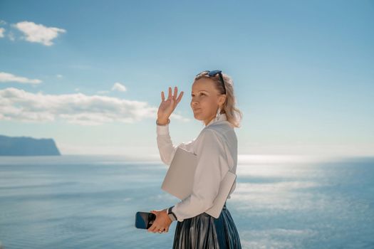 Freelance women sea working on a computer. Pretty middle aged woman with computer and phone outdoors with beautiful sea view. The concept of remote work