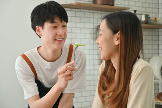Smiling asian man feeding vegetable salad to his girlfriend. Family moments, healthy lifestyle concept.