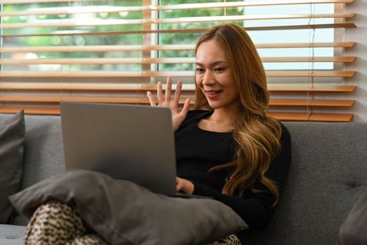 Happy woman in casual clothes having video calling, communicating online via laptop at home.